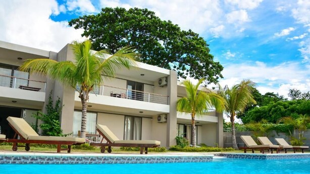 Un hotel moderno con piscina, sillones de descanso y palmeras.