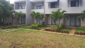 Un edificio moderno de varios pisos con techo plano, ventanas amplias y un césped cuidado con palmeras.