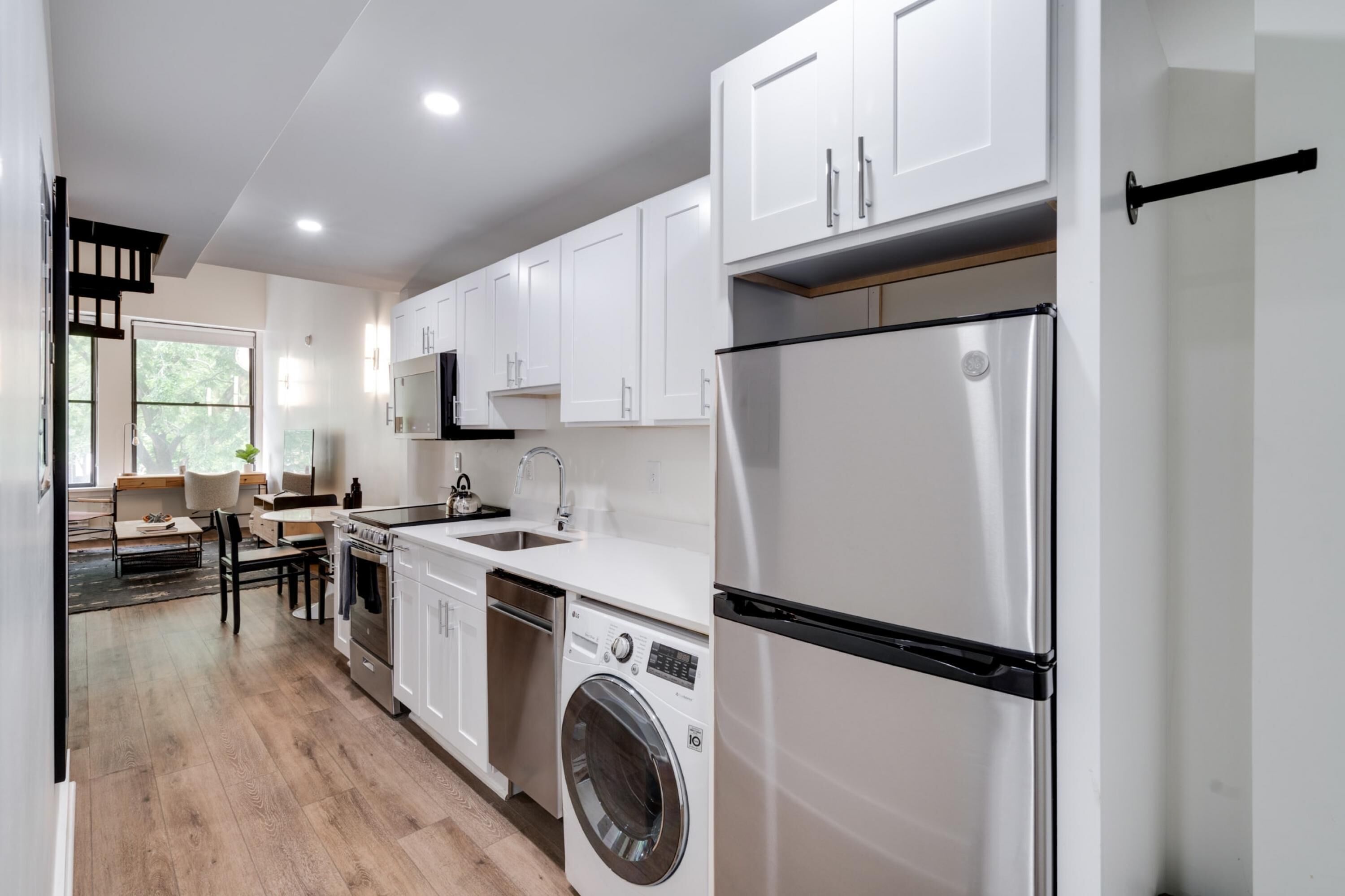 Une cuisine moderne avec des armoires blanches, des appareils en acier inoxydable et un lave-linge et un sèche-linge intégrés.