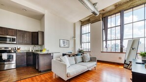 A modern kitchen with stainless steel appliances, a grey sofa, and large windows offering a city view. - Sosuite 2BR Penthouse w W D Gym On-site Bar (Philadelphia)