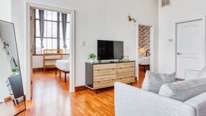 A modern living room with a flat-screen TV, a grey sofa, and a wooden cabinet. - Sosuite 2BR Penthouse w W D Gym On-site Bar (Philadelphia)