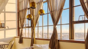 A cozy living room with a sofa, a table, and a view of the city through large windows. - Sosuite 1BR Penthouse w W D Gym On-site Bar (Philadelphia)
