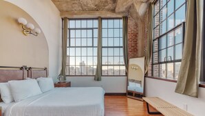 A bedroom with a large bed, a bench, a mirror, and a window with a city view. - Sosuite 2BR Penthouse w Balcony W D Gym (Philadelphia)