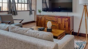 A modern living room with a large flat-screen TV, a wooden cabinet, a sofa, and a lamp. - Sosuite 2BR Penthouse w Balcony W D Gym (Philadelphia)
