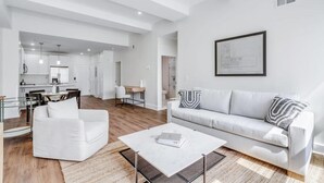 A modern living room with a white sofa, a coffee table, and a dining area with a table and chairs. - Sosuite 2BR Apt w Park View, W/d, Gym, Lounge (Philadelphia)