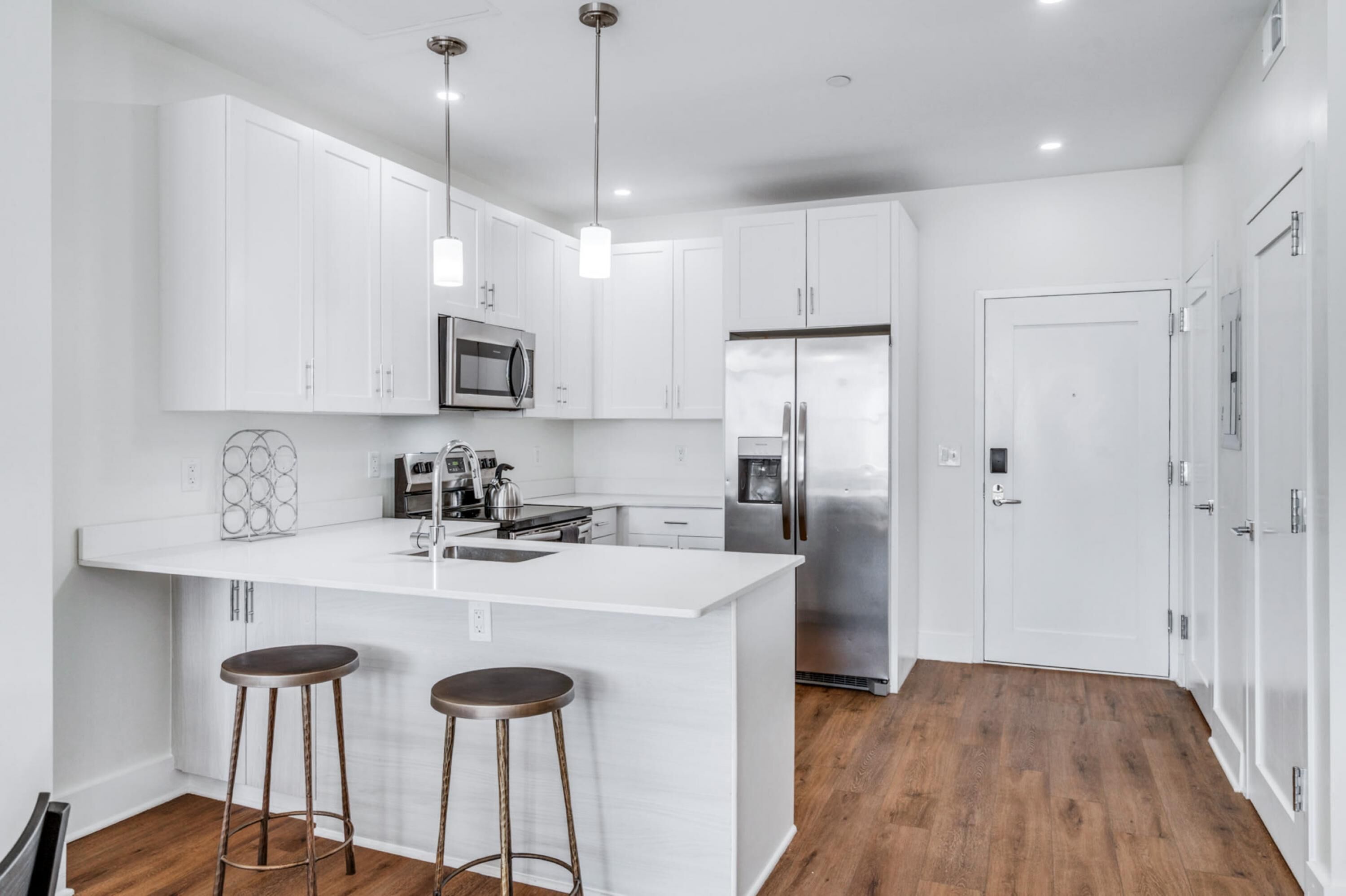 A modern kitchen with white cabinetry, a central island with stools, stainless steel appliances, and pendant lighting.