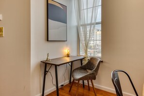 A corner room with a wooden desk, a chair, a lamp, and a large window with a view of buildings. - Stairway 3BR Apt w W D Ideal for Groups (Philadelphia)