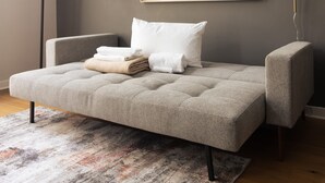 A modern bedroom with a grey upholstered bed, a white pillow, and neatly folded towels. - Sosuite 2BR Loft w W/d, Shared Roofdeck (Philadelphia)
