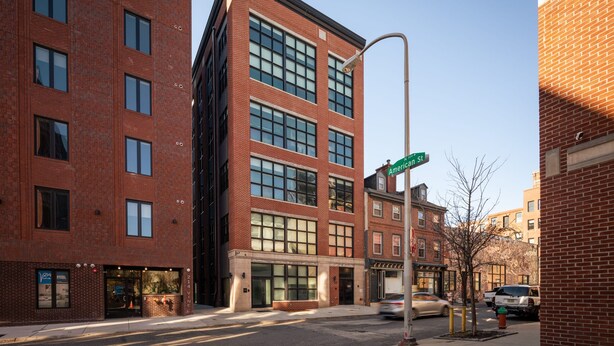 A multi-story brick building with large windows, a street sign, and parked cars. - Sosuite 2BR Loft w W/d, Shared Roofdeck (Philadelphia)