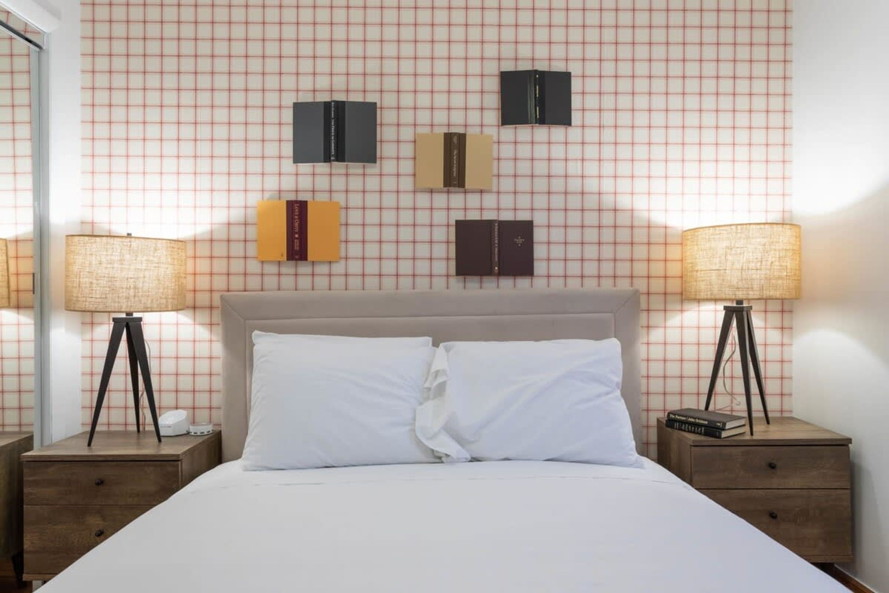 Een netjes ingerichte hotelkamer met een geruit wandpaneel, een groot bed met witte lakens, twee nachtkastjes met lampen en enkele boeken aan de wand.
