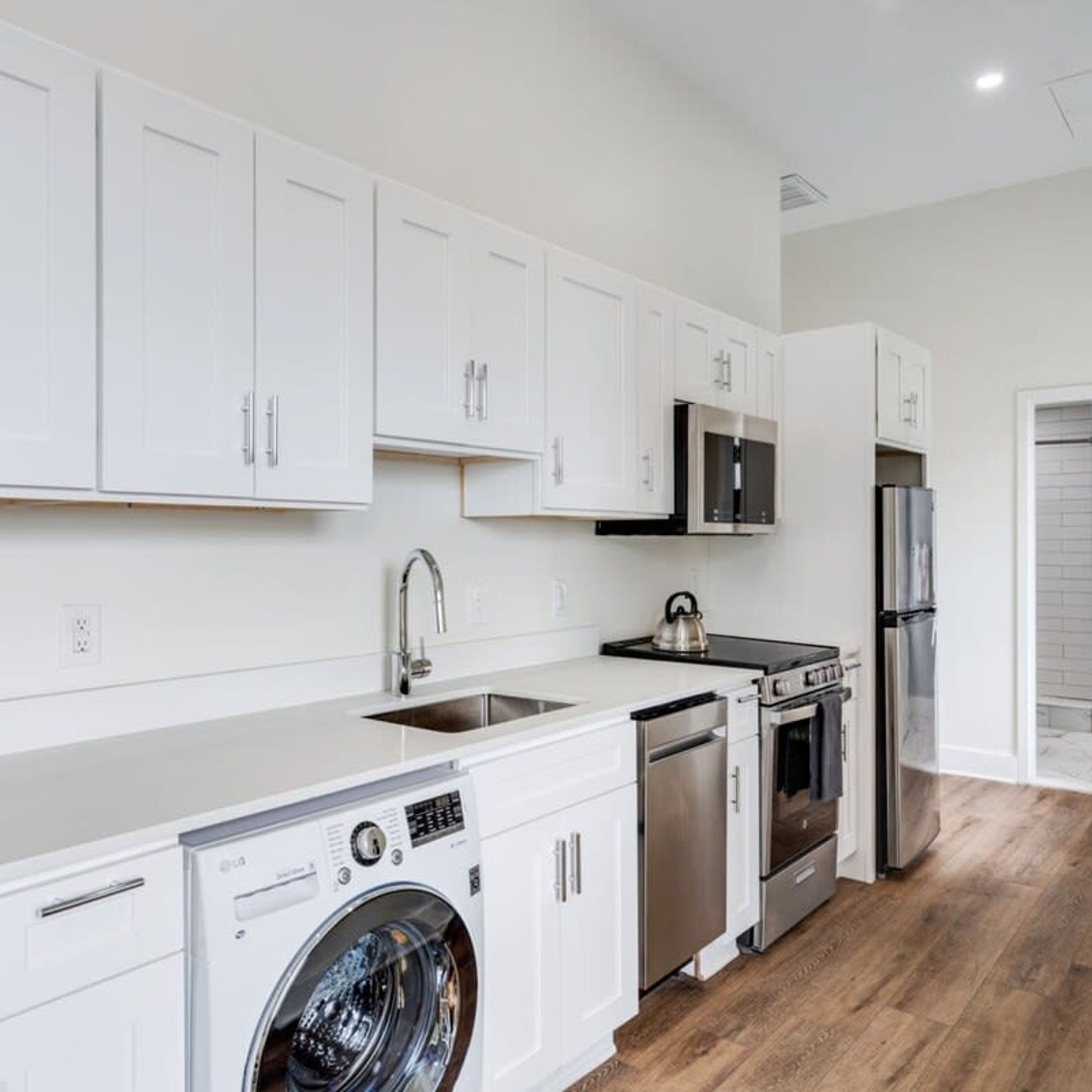 A modern kitchen with white cabinets, stainless steel appliances, and a built-in washer and dryer.