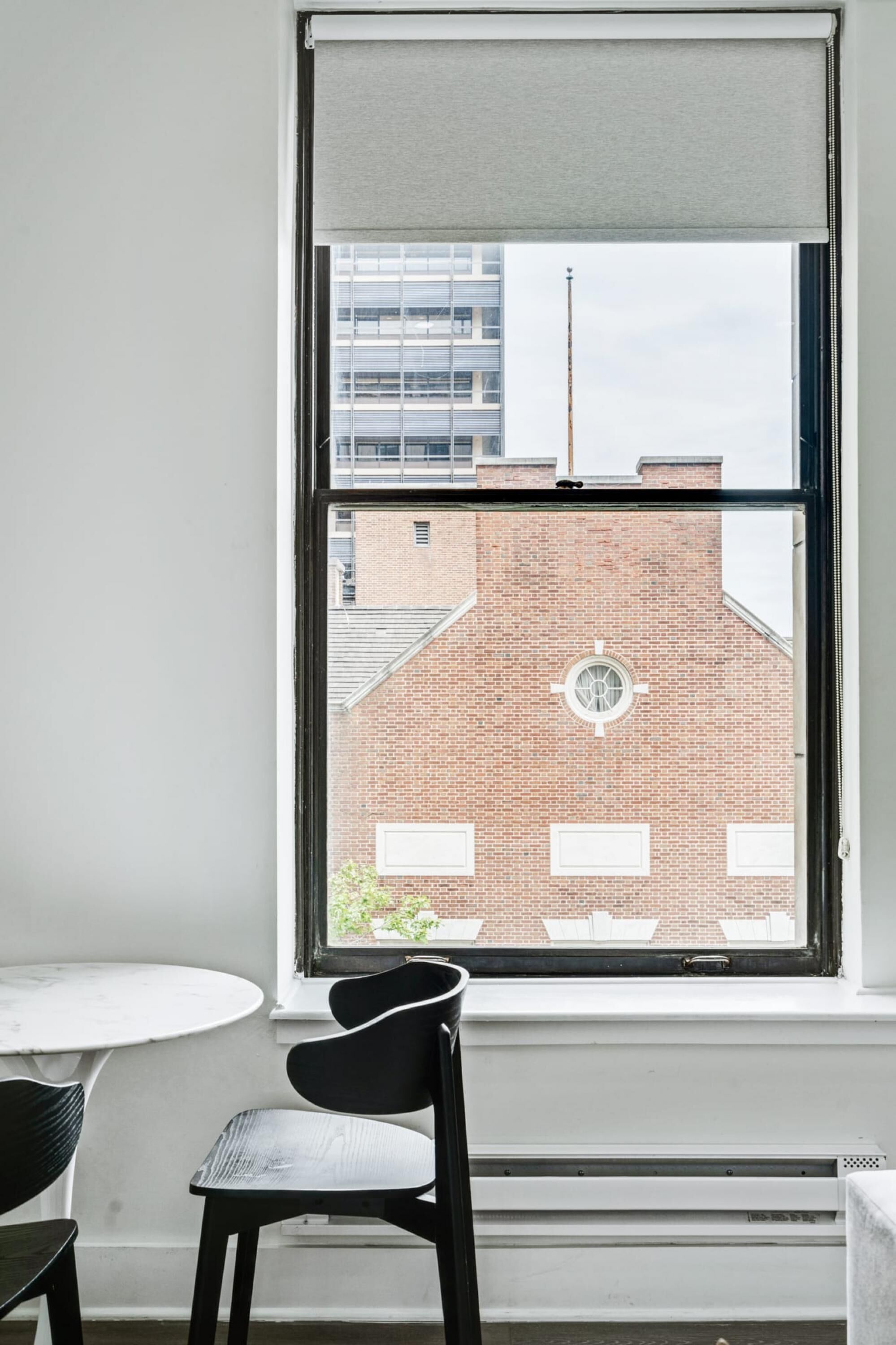 A room with a large window, a round table, and a black chair.