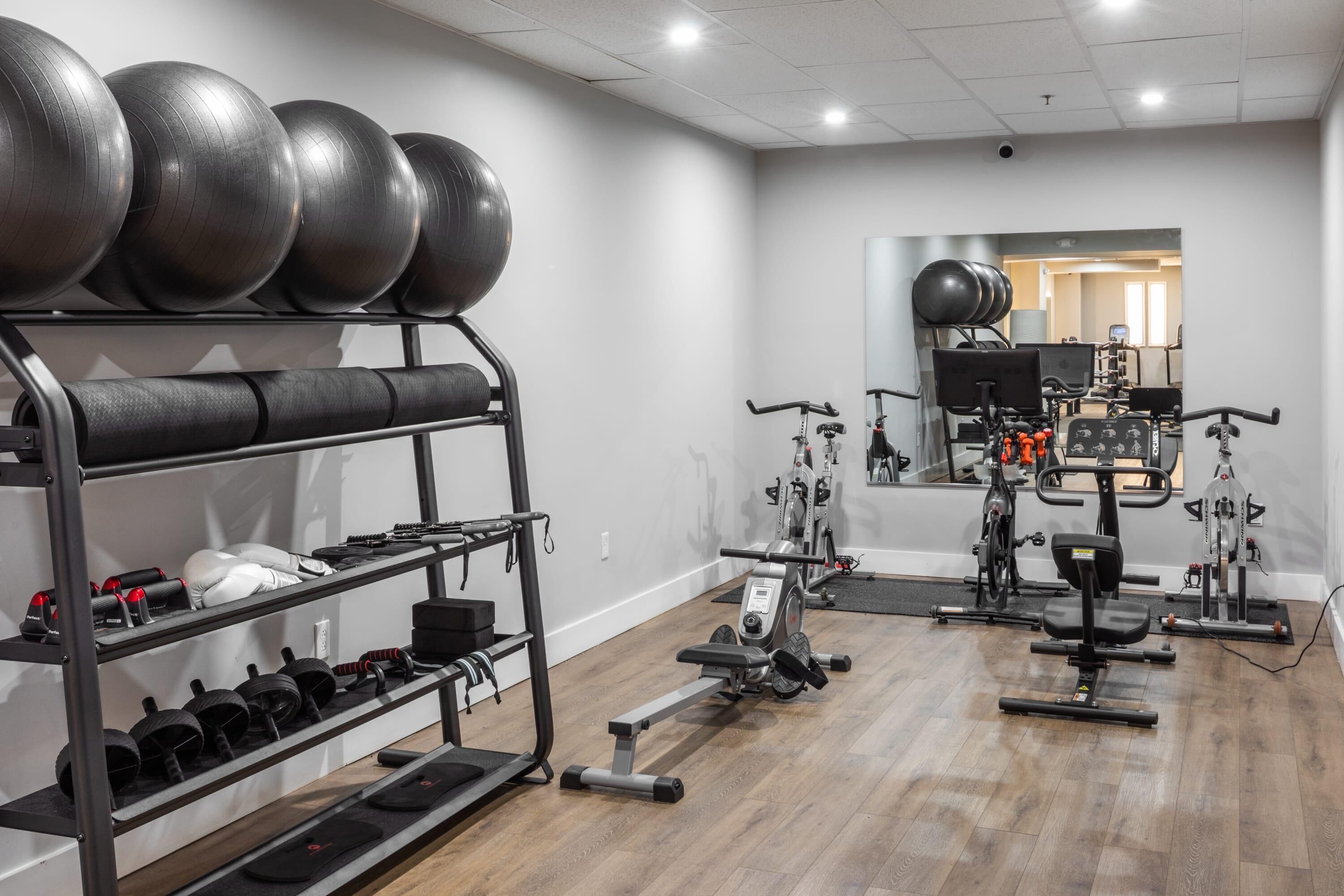 A gym with exercise equipment, a mirrored wall, and a wooden floor.