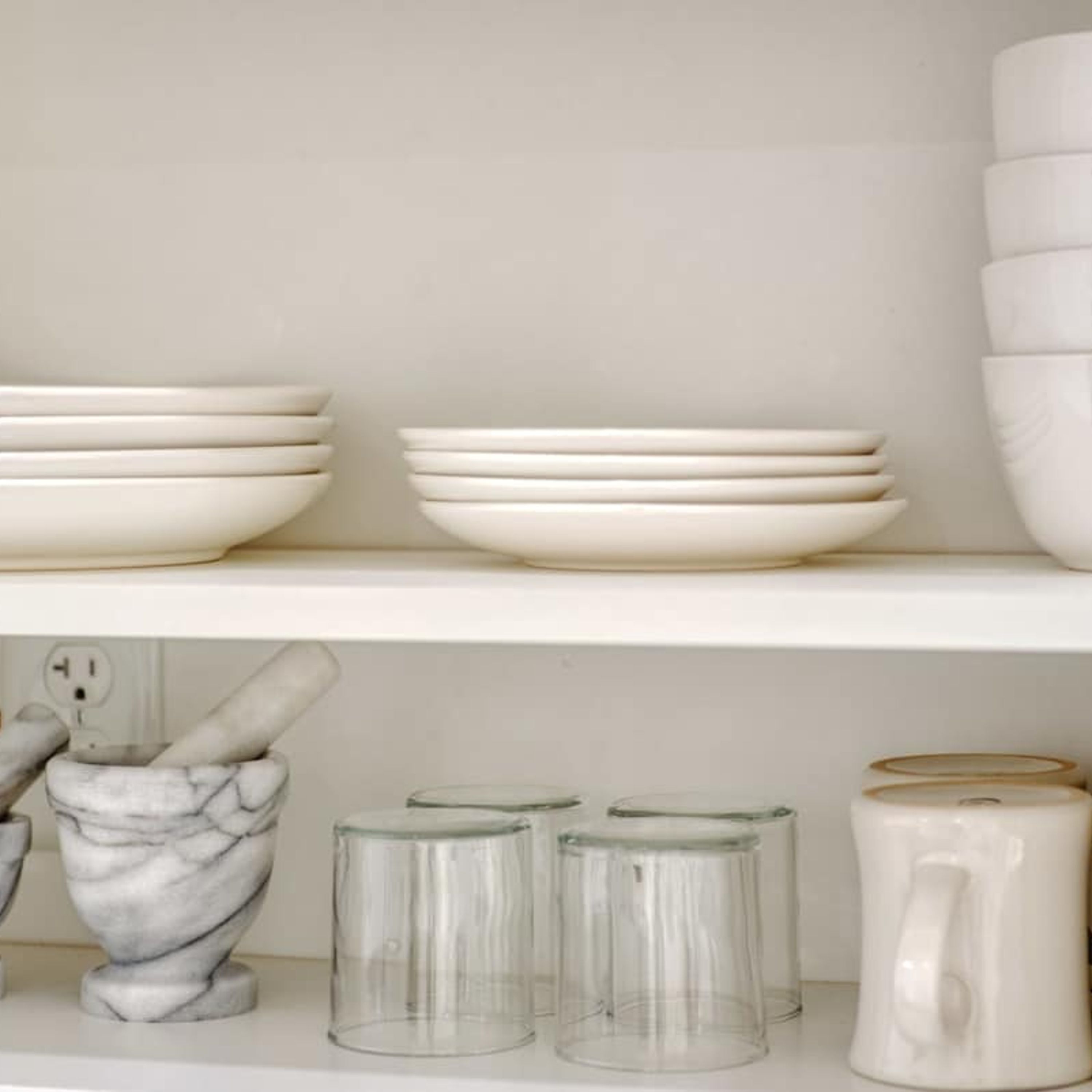 A kitchen shelf with white plates, bowls, and a marble sculpture.