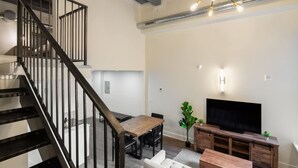 A modern living room with a staircase, a dining area, and a TV. - Sosuite 2BR Loft w Shared W/d, Gym, Lounge (Philadelphia)