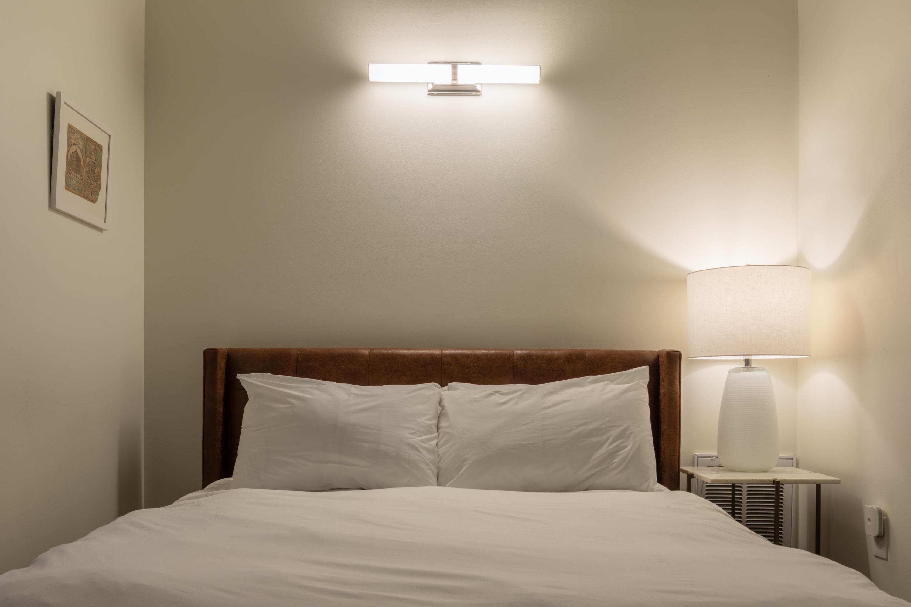 A neatly made bed with white linens, a wooden headboard, and a bedside lamp.