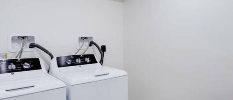 A laundry room with two white washing machines and a control panel.