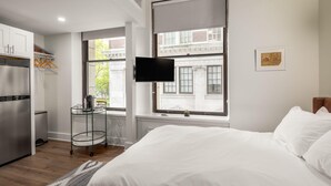 A modern hotel room with a large bed, a television mounted on the wall, and a window with a view of a building. - Sosuite Micro Studio w Shared W D Gym Lounge (Philadelphia)