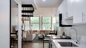 A modern kitchen with white cabinets, a stainless steel sink, and a kettle on the counter.