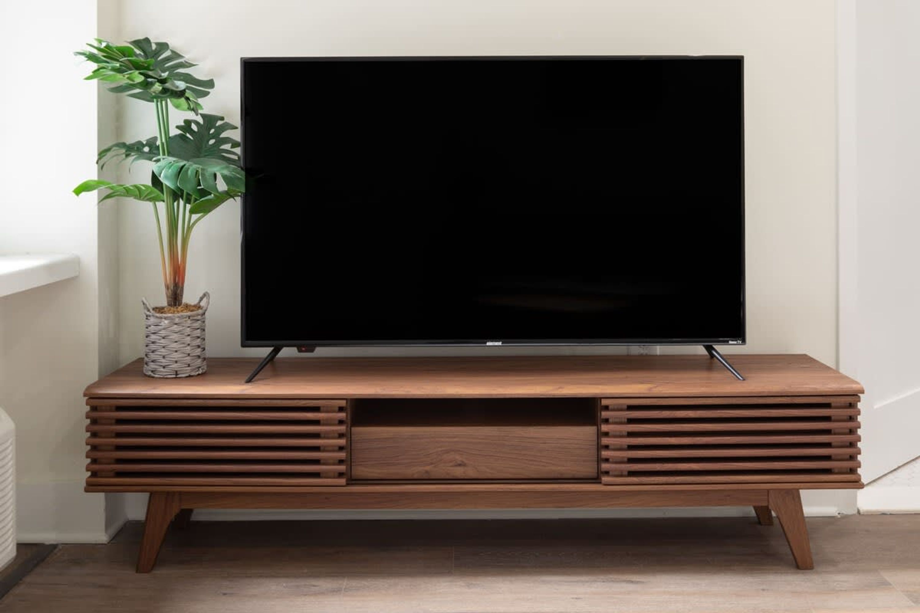 A flat-screen TV on a wooden TV stand with a plant beside it.