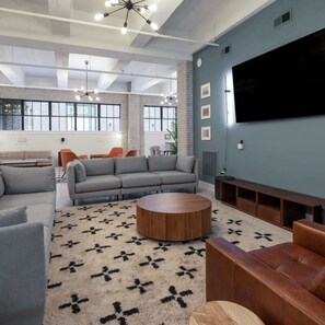 A modern living room with a grey sofa set, a round wooden coffee table, and a large flat-screen TV mounted on the wall. - Sosuite 1BR Apt Acc w W D Gym Lounge (Philadelphia)