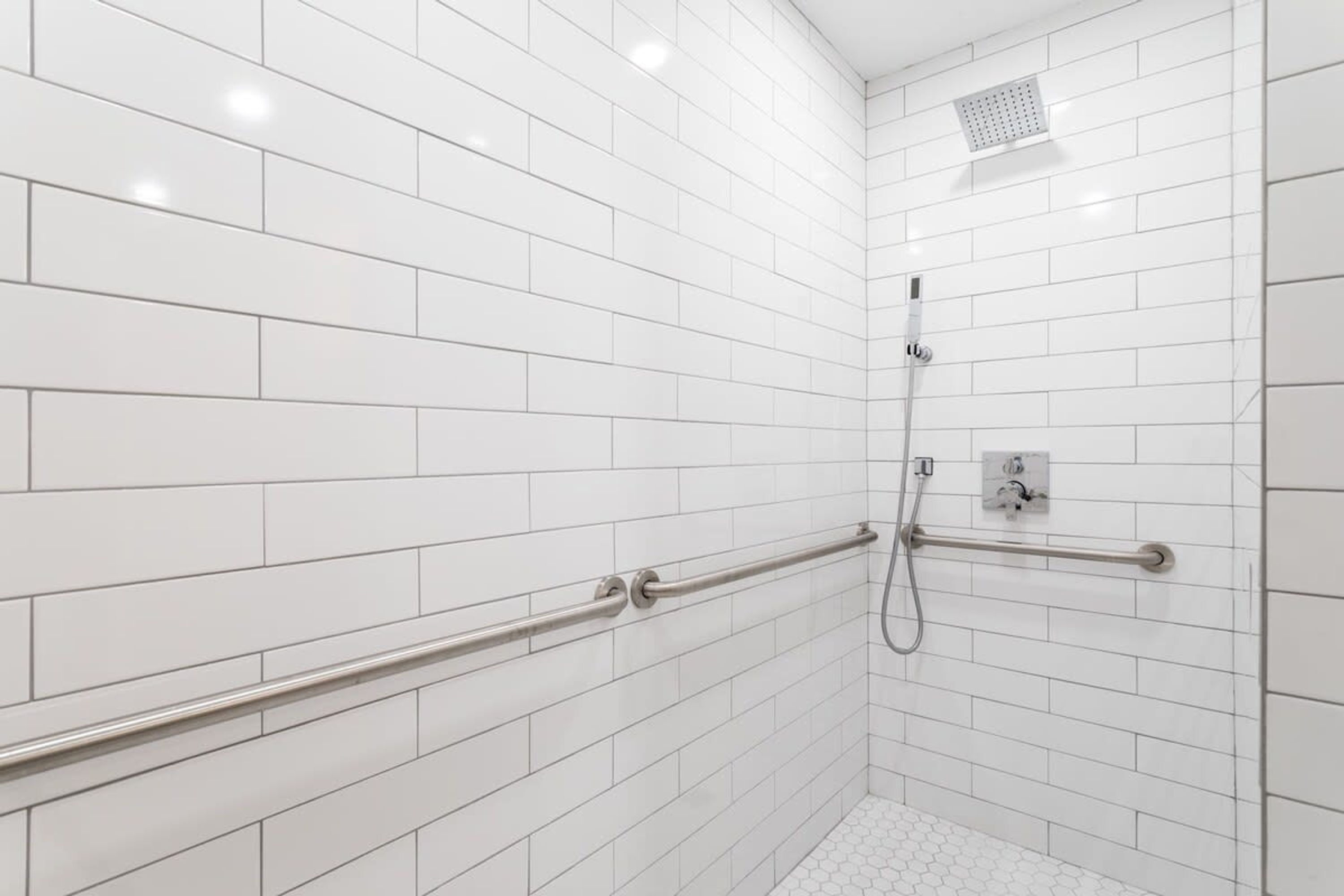 A white-tiled shower area with a handheld showerhead, a handheld showerhead, and a handheld showerhead.