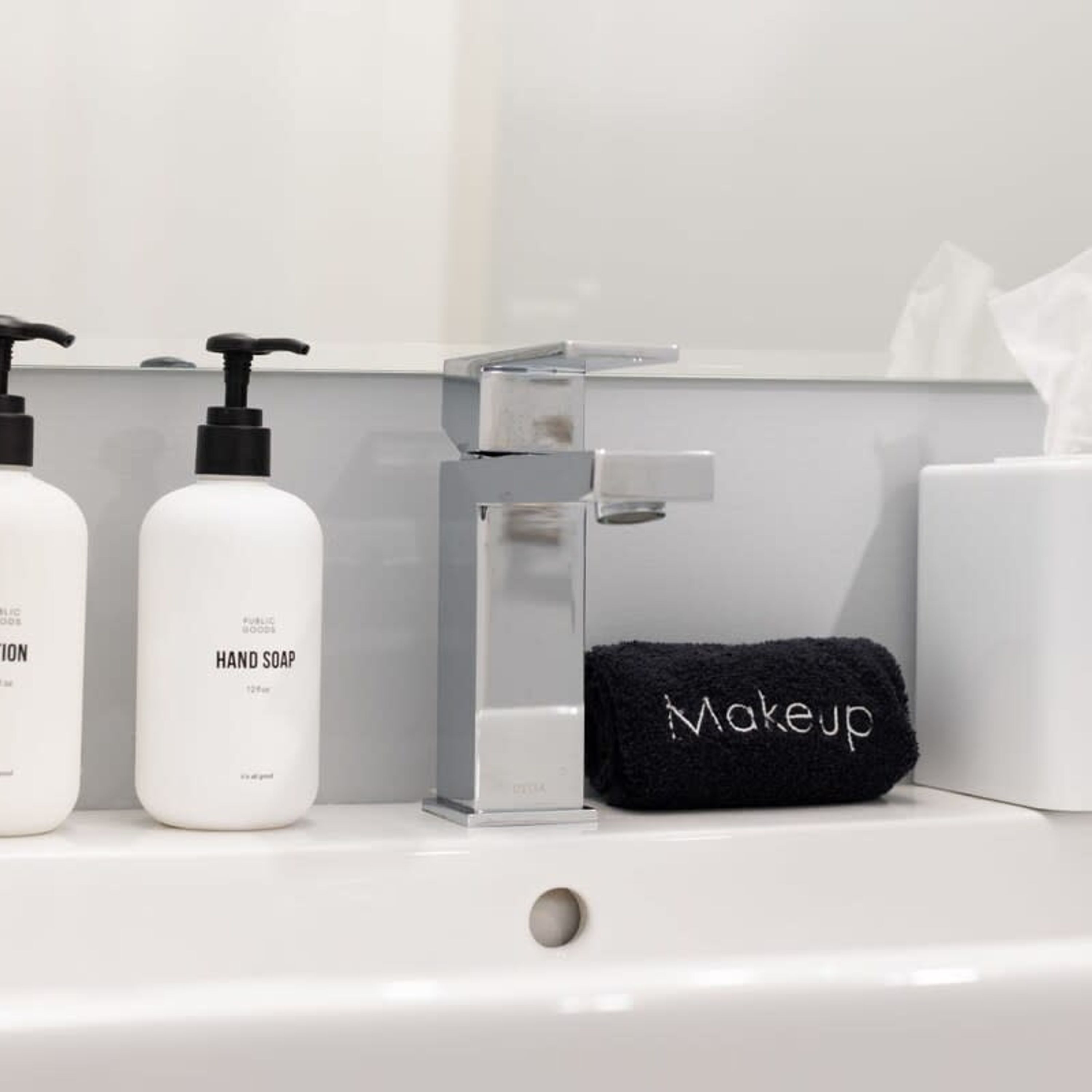 A bathroom sink with two hand soap bottles, a soap dispenser, and a black towel with "Makeup" written on it.