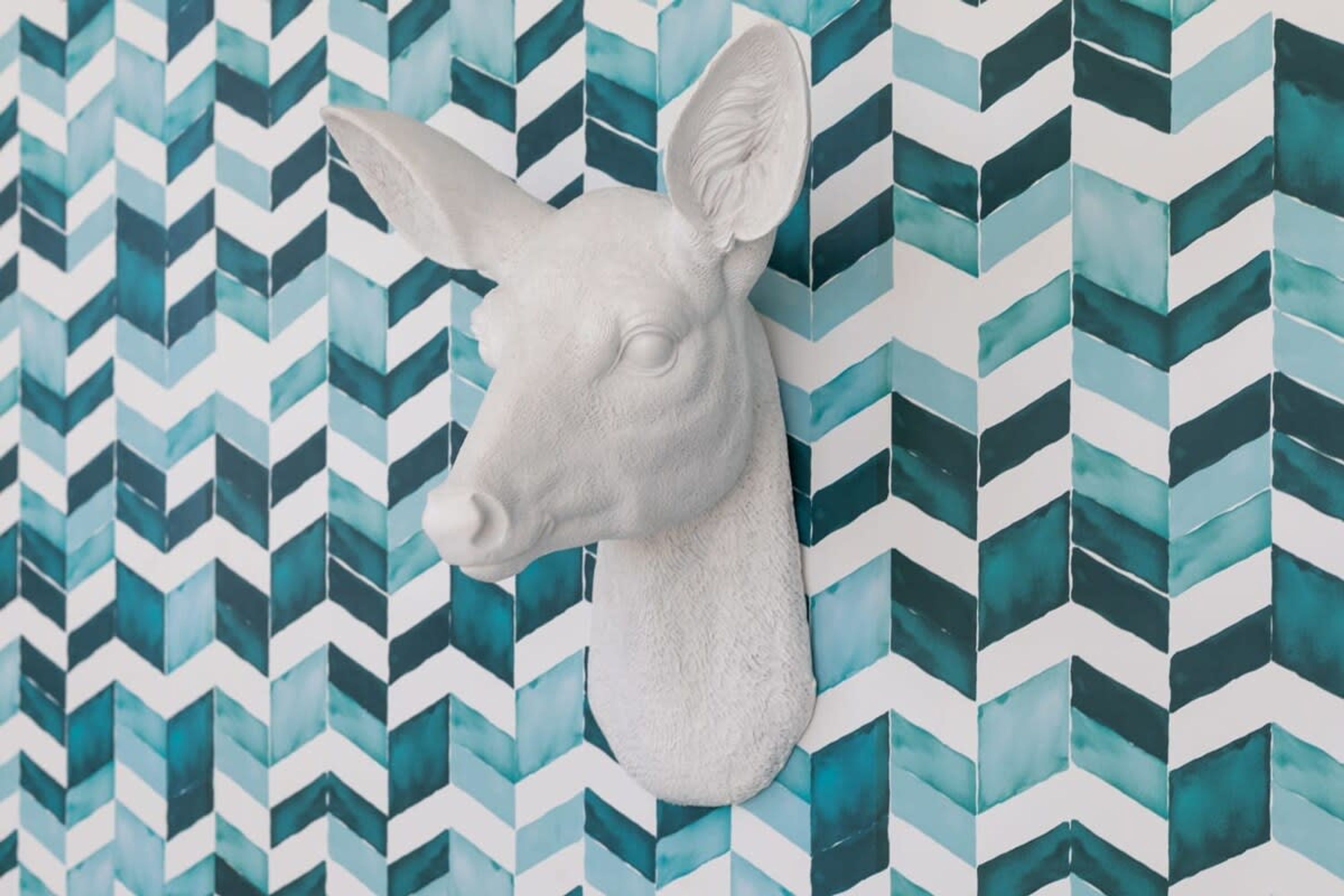A wall-mounted deer head sculpture against a chevron-patterned tile background.