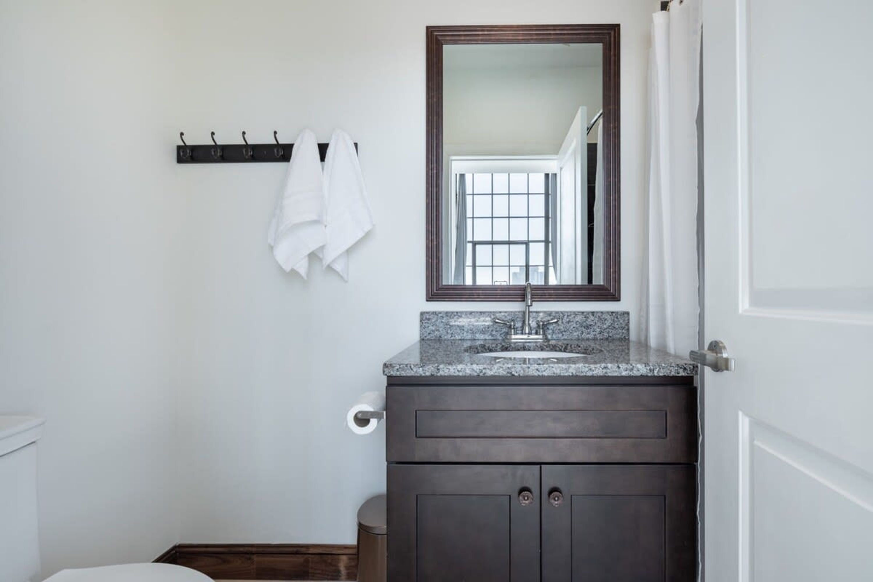 A bathroom with a dark wooden vanity, a granite countertop sink, and a large mirror above it. There are towels hanging on a rack and a toilet visible.