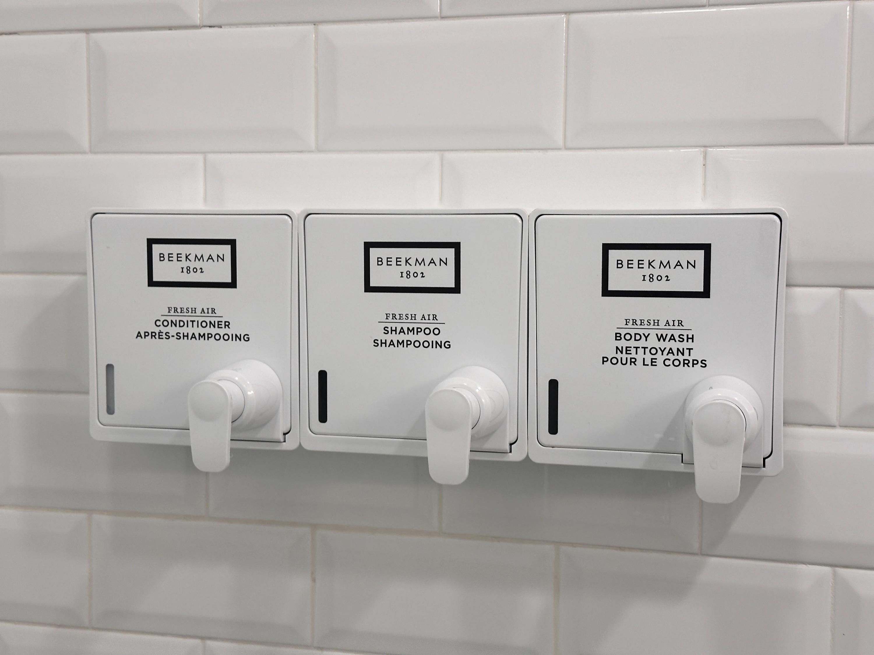Three wall-mounted dispensers labeled 'BEEKMAN 1802' for fresh air conditioner, shampoo, and body wash.