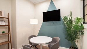 A conference room with a white table, four grey chairs, a floor lamp, a TV on the wall, a bookshelf, and a potted plant. - Sosuite 1BR Loft w Shared W/d, Gym, Lounge (Philadelphia)