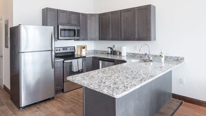 A modern kitchen with dark cabinets, stainless steel appliances, and a granite countertop. - Sosuite 2BR Penthouse w W D Gym On-site Bar (Philadelphia)
