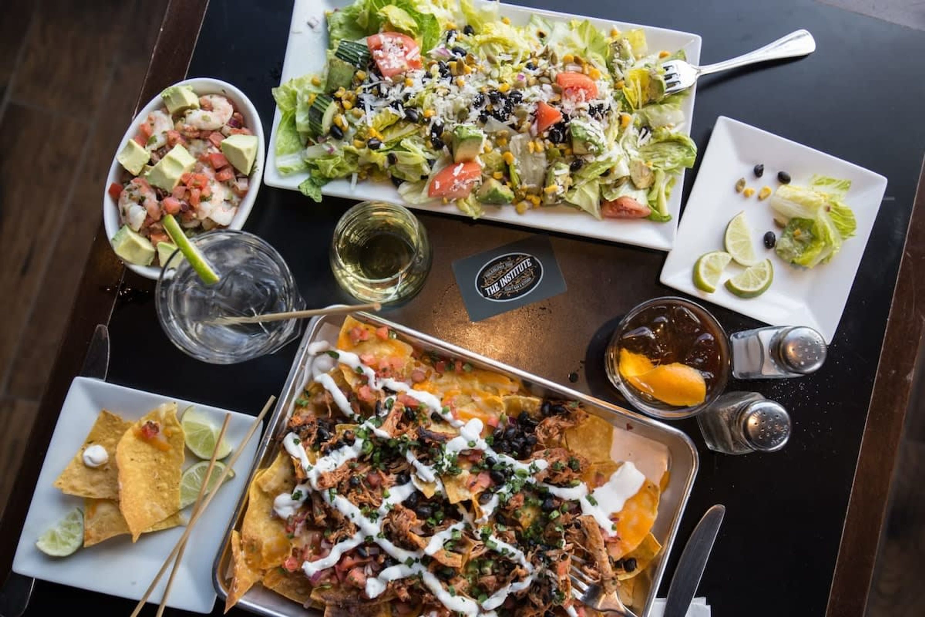 Una mesa con varios platos, incluyendo nachos, una ensalada y un bol de coctel de camarones.