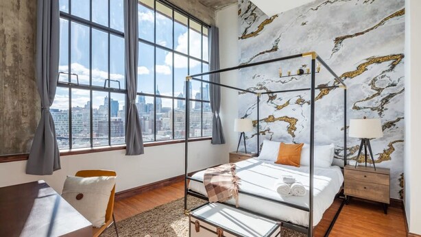A modern bedroom with a city view, a four-poster bed, and a marble-patterned wall. - Sosuite 2BR Penthouse w W D Gym On-site Bar (Philadelphia)