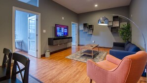 A modern living room with a flat-screen TV, a sofa, a coffee table, and a dining area with chairs.
