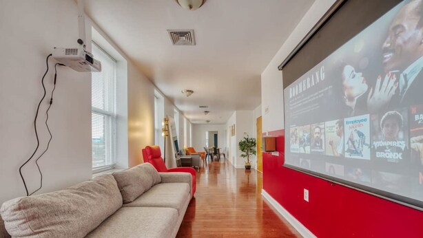 A modern hotel corridor with a red accent wall, a large screen displaying content, and a sofa along the wall.