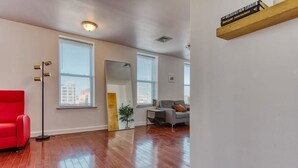 A spacious living room with hardwood floors, a red sofa, a gray couch, and a tall floor lamp.