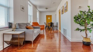 A modern living room with a grey sofa, orange armchair, and a dining table with chairs.
