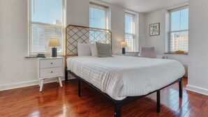 A bedroom with a bed, two bedside tables, a nightstand, and a window with blinds.