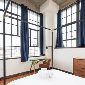 A modern hotel room with large windows, a bed, a desk, and a chair.