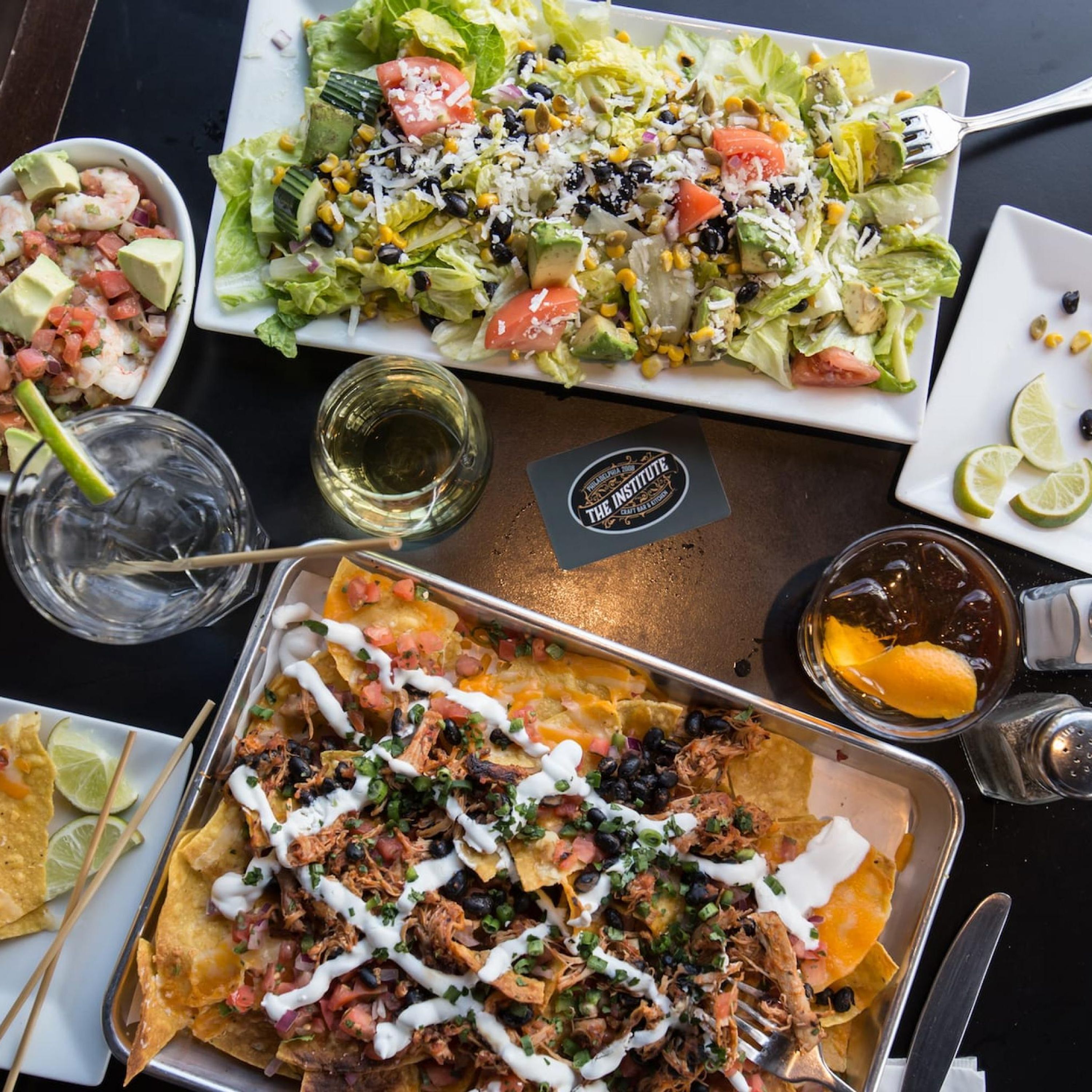 A table with a variety of dishes including nachos, a salad, and a shrimp dish, along with drinks and condiments.