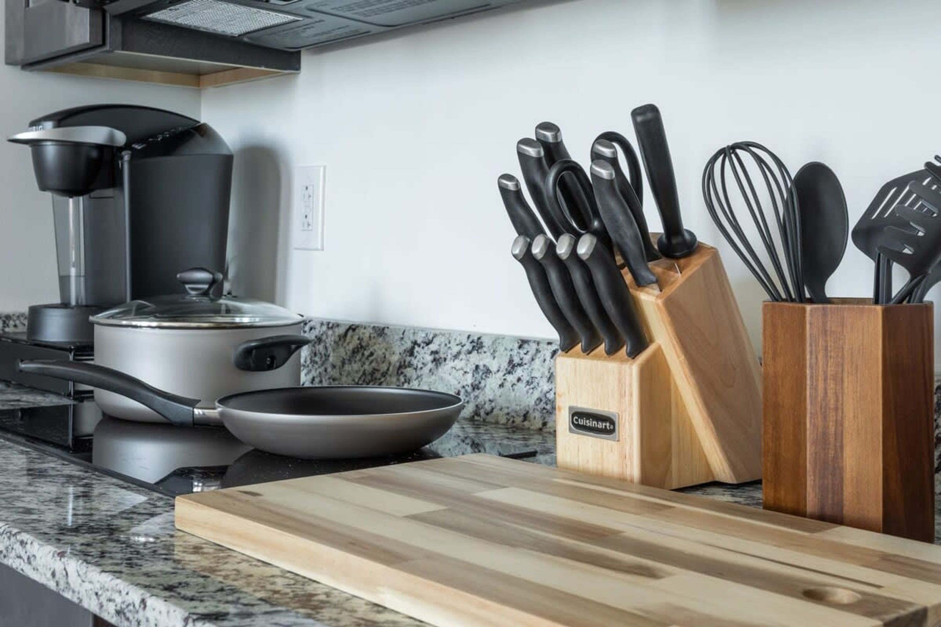Una cocina con cafetera, sartén, tabla de cortar y bloque para cuchillos.