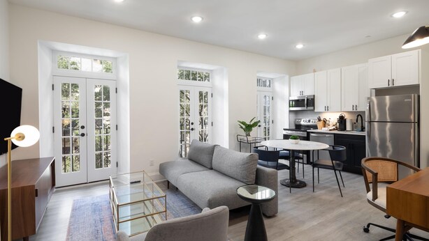 A modern living room with a grey sofa, a glass coffee table, and a dining area with a round table and chairs. - Sosuite Juliet Balcony 1BR Apt w W D Desk (Philadelphia)