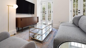 A modern living room with a glass coffee table, grey sofa, and a flat-screen TV mounted on the wall. - Sosuite Juliet Balcony 1BR Apt w W D Desk (Philadelphia)