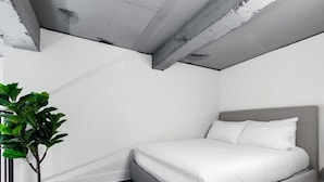 A bedroom with a bed, a potted plant, and exposed concrete beams. - Sosuite 2BR Loft w W/d, Gym, Lounge (Philadelphia)