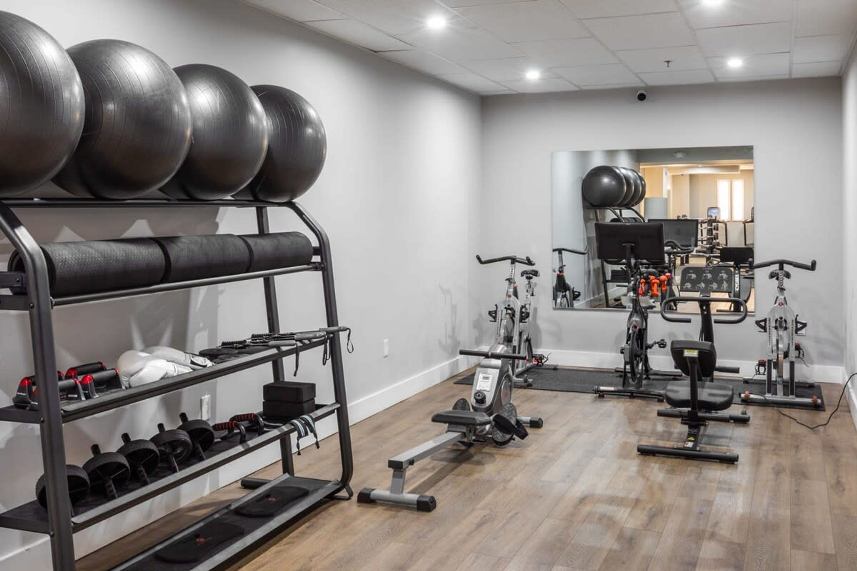A gym with exercise equipment, a mirrored wall, and a wooden floor.