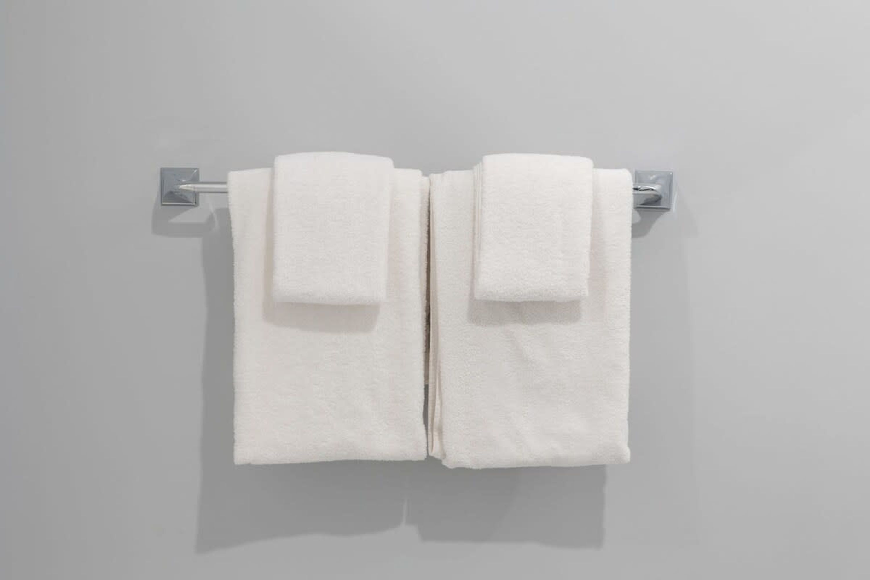 A pair of white towels hanging on a metallic towel rack against a plain wall.