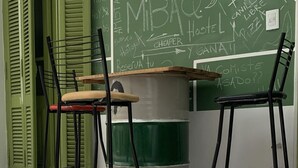 A room with a green chalkboard wall, two black chairs, a wooden table, and a green bucket. - MiBAQ Hostel (Buenos Aires)