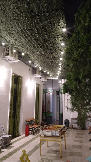 An outdoor seating area with a ceiling covered in artificial leaves, a bench, and a table with various items. - MiBAQ Hostel (Buenos Aires)