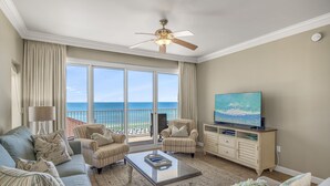 A spacious living room with a large TV, comfortable seating, a ceiling fan, and a view of the ocean. - Gulf Front with Beach Views & Large Balcony (Miramar Beach)